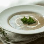 creamy mushroom soup in a white ceramic bowl, garnished with fresh parsley and a swirl of cream